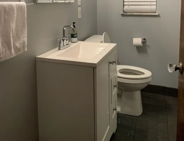 Small bathroom with white vanity sink, toilet, towel, and gray walls.