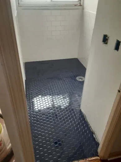 Small unfinished bathroom with black shower pan liner and white tiled walls